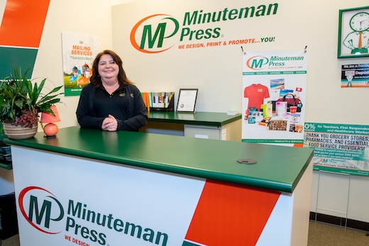 Image of Minuteman Press Owner Diana Renollet in front of the minuteman press logo