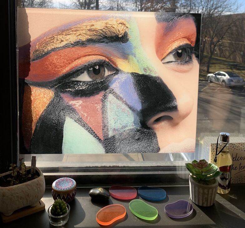 Image featuring a painting of a white woman's face with red, orange, blue, black and teal mosaic makeup 
